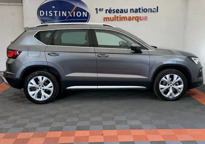 Vue de profil côté gauche d'un SEAT Ateca gris clair 2023 avec jantes alliage et barres de toit chromées.