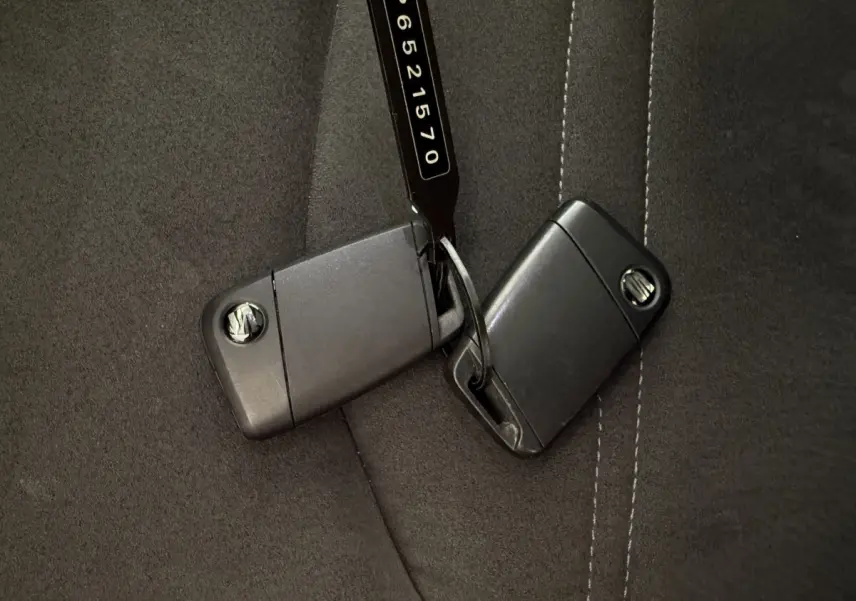 Gros plan sur deux clés noires SEAT posées sur un siège en tissu gris foncé avec surpiqûres blanches.