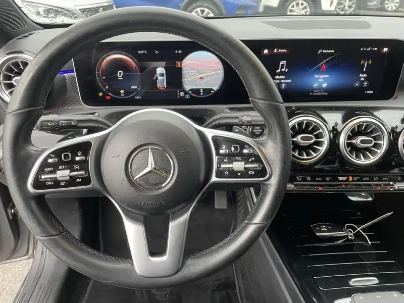 Vue intérieure centrée sur le volant et le tableau de bord numérique d'une Mercedes Classe A gris foncé de 2019.