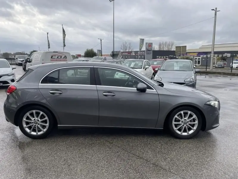 Vue de profil côté gauche d'une Mercedes Classe A 200 gris foncé métallisé, stationnée sur parking humide.