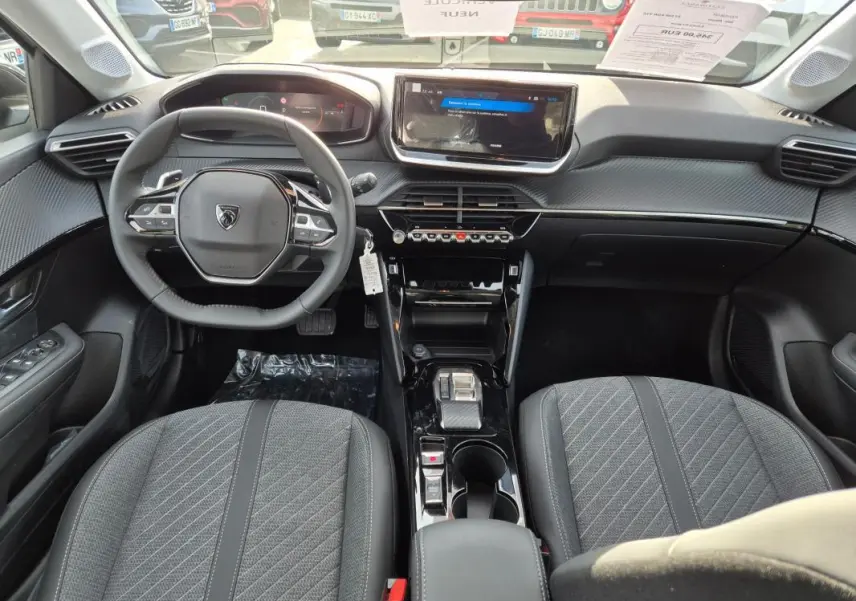 Vue intérieure avant de la Peugeot 208 Hybrid 110 Allure 2025, mettant en valeur le volant compact, l'écran tactile et les sièges gris.