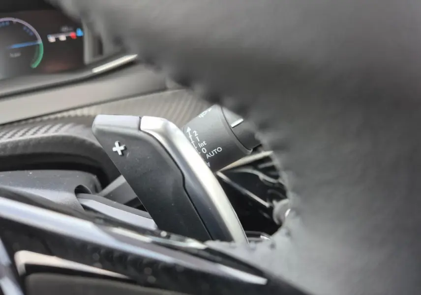 Gros plan sur la palette de changement de vitesse "+" derrière le volant du Peugeot 208 blanc, intérieur moderne.