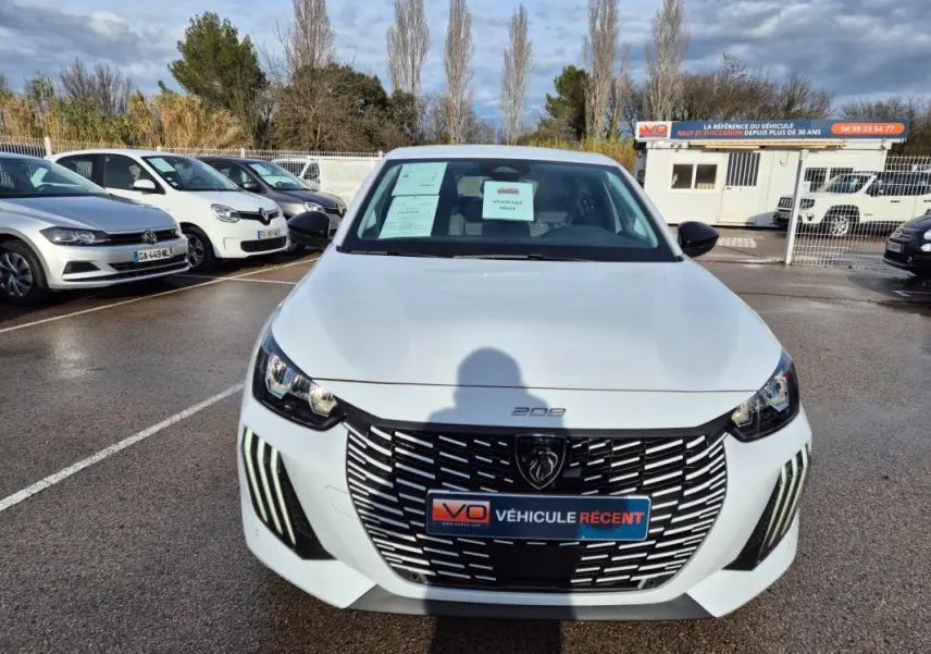 Vue avant d'une Peugeot 208 Hybrid 110 e-DCS6 Allure blanche avec calandre noire et feux LED diurnes verticaux.