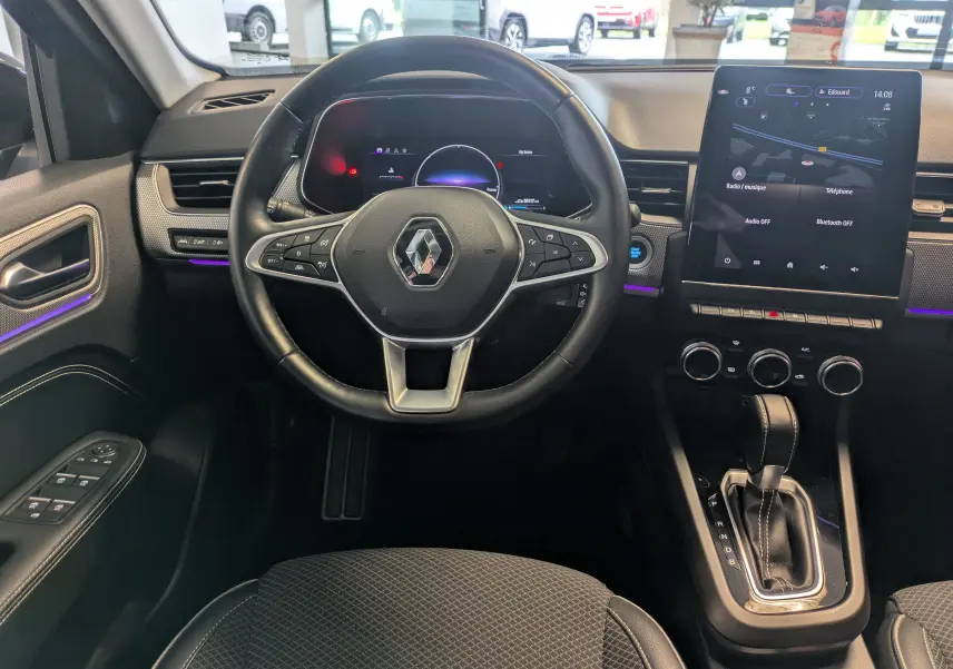 Vue intérieure centrée sur le volant et la console centrale d’une Renault Arkana noire, avec écran tactile et levier de boîte automatique.