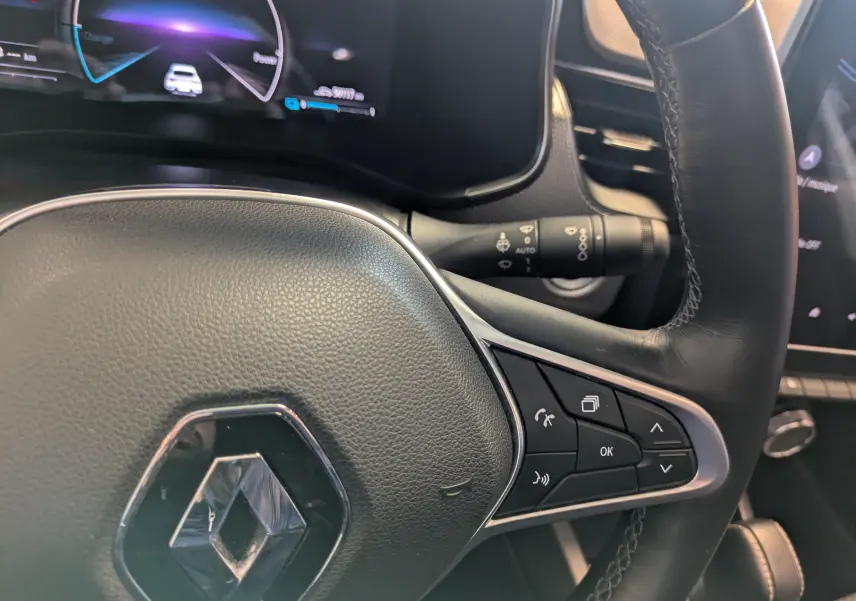 Gros plan sur le volant cuir noir du Renault Arkana 2023, avec commandes intégrées et tableau de bord numérique en arrière-plan.