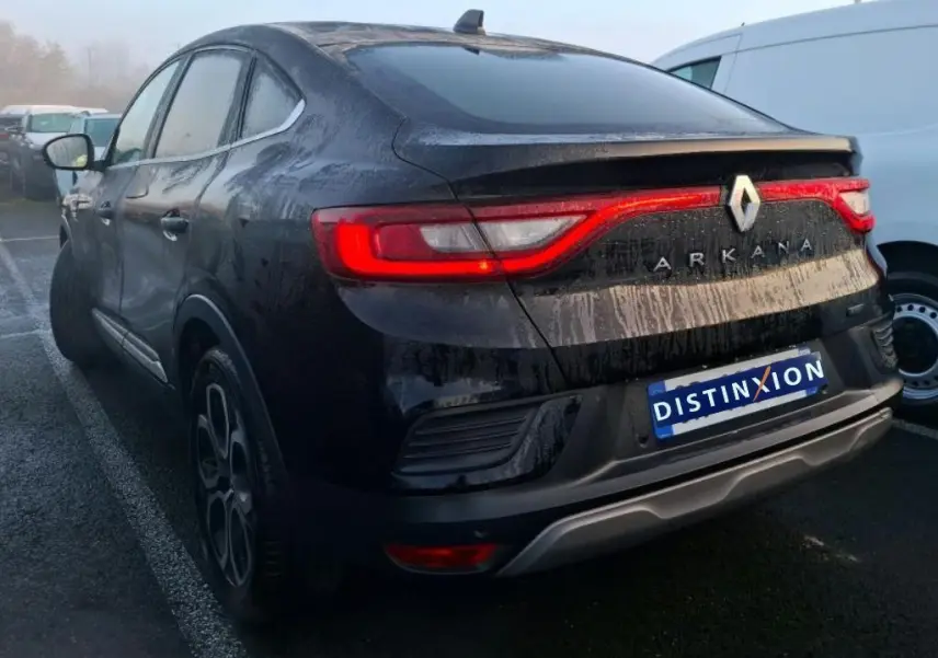 Vue 3/4 arrière gauche d'un Renault Arkana noir métal 2023 avec feux arrière allumés et logo visible.