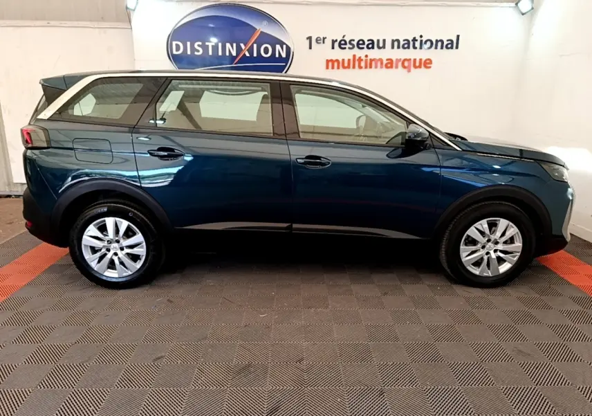 Vue de profil côté gauche d’un Peugeot 5008 bleu 2021 garé en intérieur avec jantes argentées et toit noir.