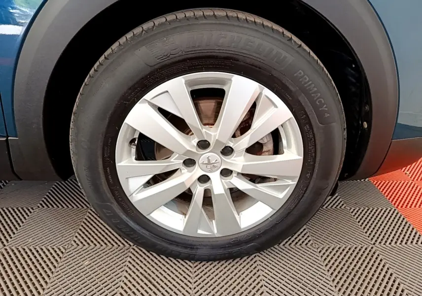 Gros plan sur la roue avant gauche d’un Peugeot 5008 bleu avec jante alliage argentée et pneu Michelin.
