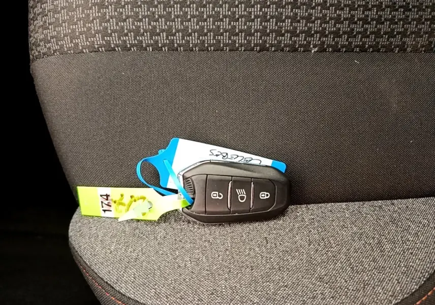 Gros plan sur la clé noire du Peugeot 5008 posée sur un siège tissu gris foncé à coutures rouges.
