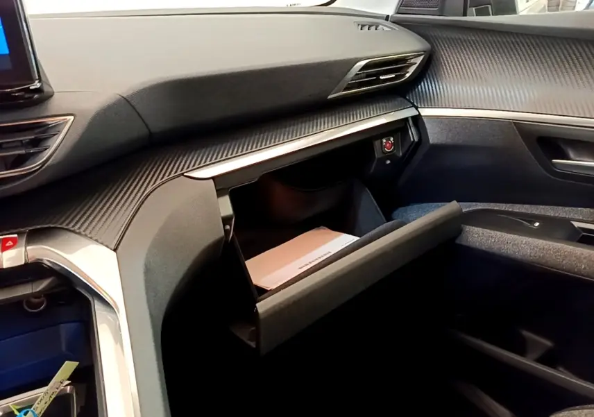 Intérieur du Peugeot 5008 2021, vue côté passager sur la boîte à gants ouverte et tableau de bord noir texturé.