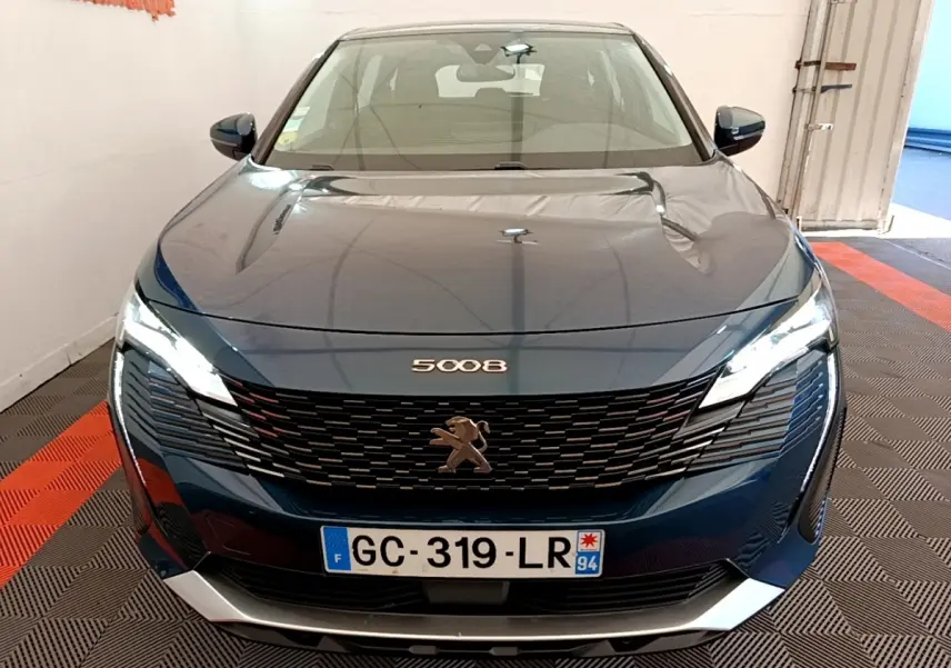 Vue frontale d’un Peugeot 5008 bleu avec calandre noire et phares LED allumés en intérieur.