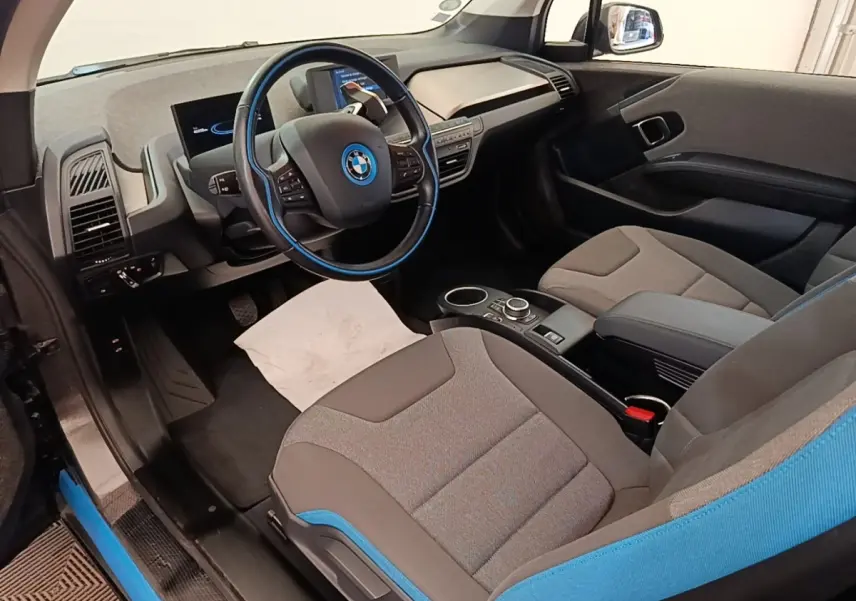 Vue intérieure côté conducteur de la BMW i3 120 Ah Atelier 2020, sièges gris avec surpiqûres bleues et volant cuir noir.