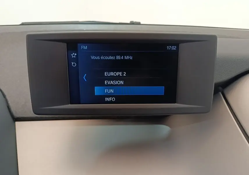 Écran central du tableau de bord de la BMW i3 noire 120 Ah Atelier, affichant les stations radio FM.