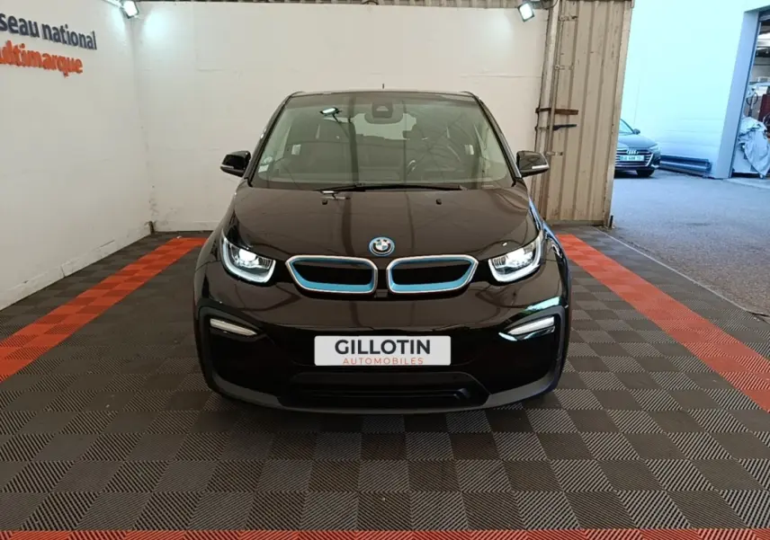BMW i3 120 Ah Atelier noire vue de face, avec calandre bleutée et phares LED allumés en intérieur showroom.