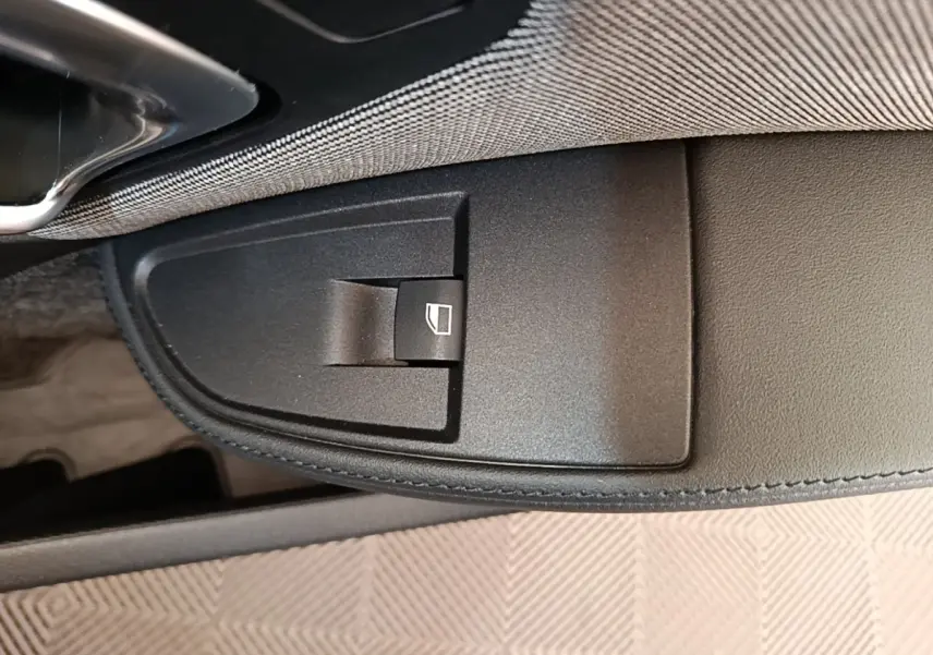 Gros plan sur le bouton de commande de lève-vitre côté conducteur dans l'intérieur noir de la BMW i3 120 Ah Atelier.