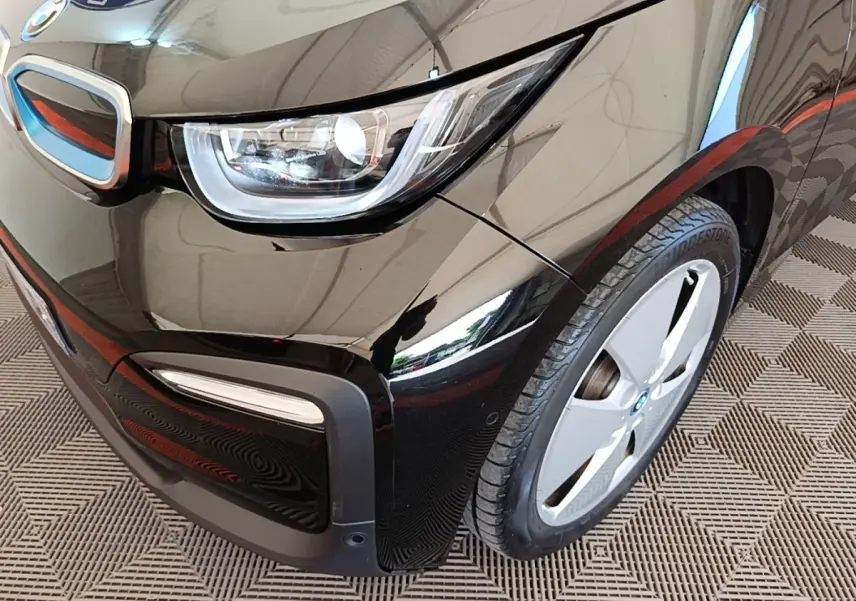 Gros plan sur l'avant droit noir d'une BMW i3 120 Ah Atelier, mettant en valeur le phare LED et la jante spécifique.