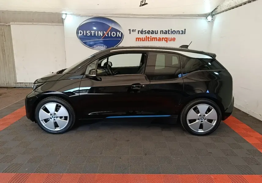 Profil côté gauche de la BMW i3 120 Ah Atelier noire, avec ses jantes distinctives et toit contrastant en intérieur fermé.