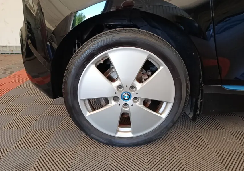 Gros plan sur la roue avant gauche argentée d’une BMW i3 noire, mettant en valeur la jante et le logo central.