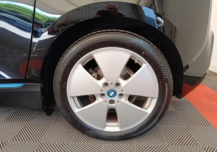 Gros plan sur la roue avant gauche d'une BMW i3 noire avec jante argentée et logo BMW au centre.