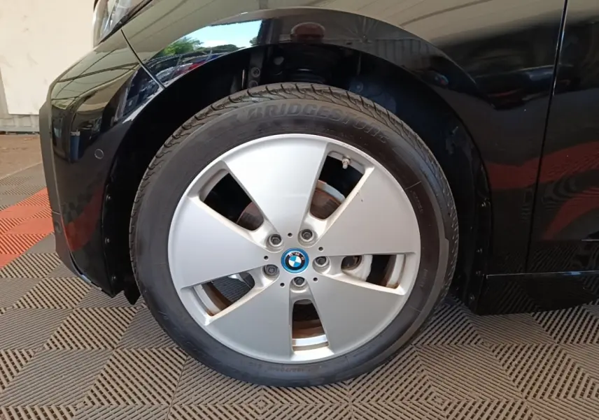Gros plan sur la roue avant gauche d’une BMW i3 120 Ah noire, mettant en valeur la jante argentée et le logo BMW central.