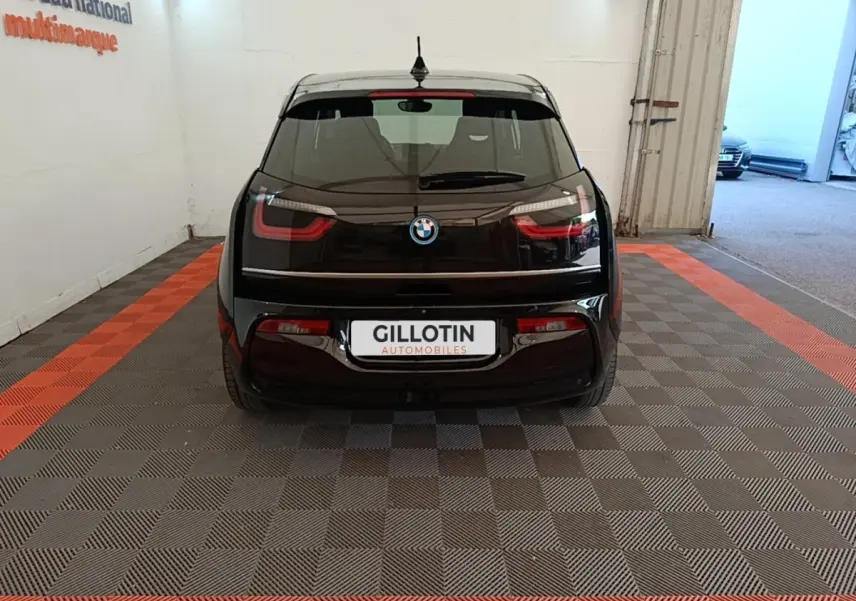 Vue arrière d'une BMW i3 120 Ah noire, stationnée en intérieur sur un sol à damiers gris et bandes orange.