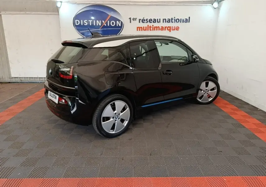 BMW i3 120 Ah Atelier noire vue de 3/4 arrière droit, dans un showroom avec sol gris et bandes rouges.