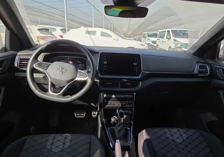 Vue intérieure avant du Volkswagen T-Cross 2025, tableau de bord noir avec volant multifonctions et écran tactile central.