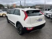 Vue 3/4 arrière droite d'un KIA Niro EV blanc 2024, version Active, avec feux arrière en forme de boomerang et jantes noires.