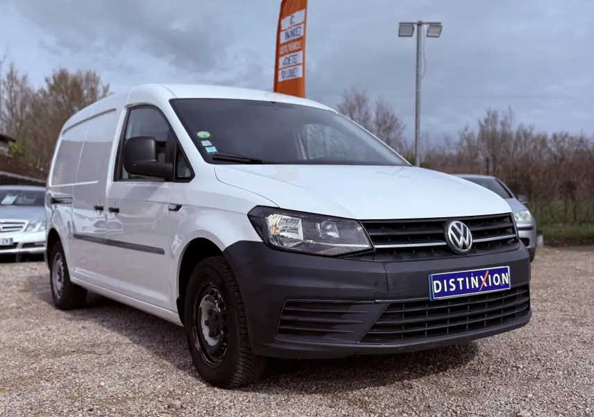 Vue 3/4 avant droit d’un utilitaire Volkswagen Caddy Maxi Long blanc avec pare-chocs noir mat sur un parking extérieur.