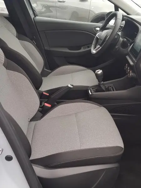 Vue intérieure côté conducteur de la Renault Clio gris 2025 avec sièges tissu bicolore et boîte manuelle visible.