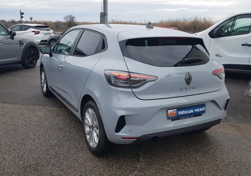 Vue 3/4 arrière droite d'une Renault Clio gris clair avec vitres surteintées et feux arrière allumés.