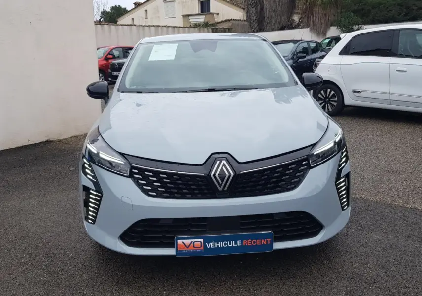 Vue de face d'une Renault Clio gris clair 2025 avec feux LED allumés et calandre noire distinctive.