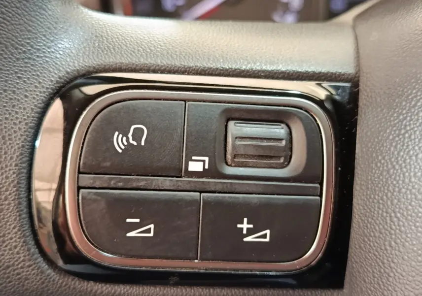 Gros plan sur les commandes de volume et reconnaissance vocale sur le volant noir de la Citroën C3 blanche.
