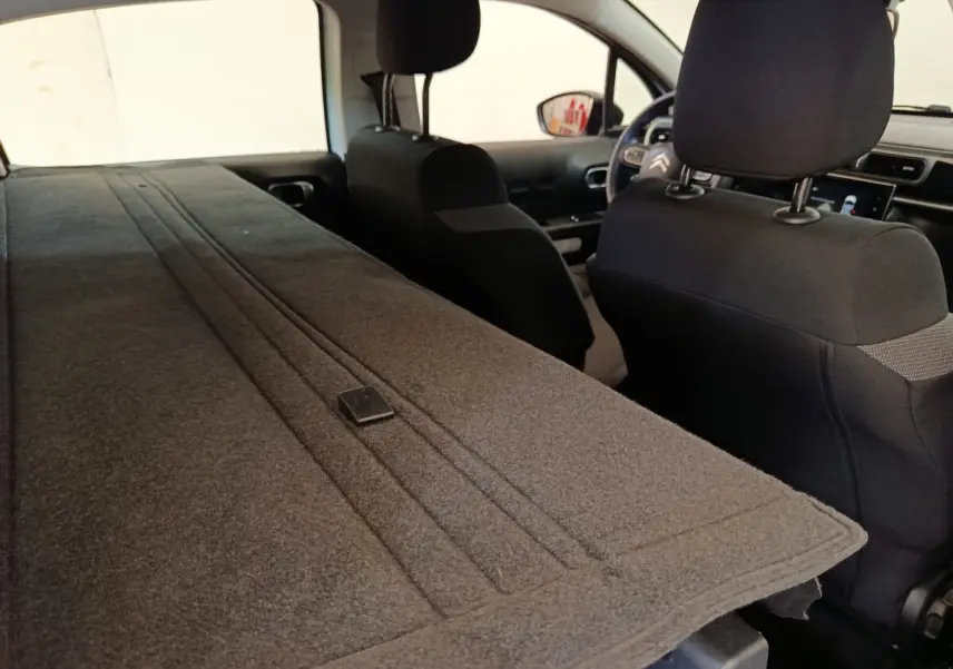Vue intérieure arrière de la Citroën C3 blanche 2022 avec banquette rabattue et sièges avant noirs.