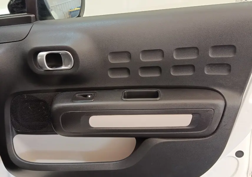 Gros plan sur la porte intérieure côté gauche de la Citroën C3 blanche, avec poignée chromée et inserts noirs texturés.
