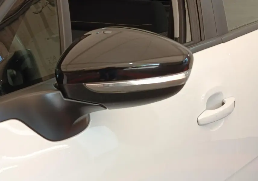 Gros plan sur le rétroviseur noir brillant côté gauche d'une Citroën C3 blanche avec poignée de porte visible.