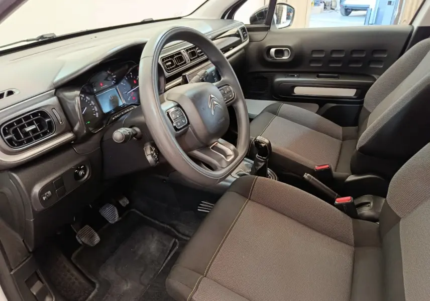Vue intérieure côté conducteur de la Citroën C3 2022, volant multifonctions, sièges tissu gris et tableau de bord noir.