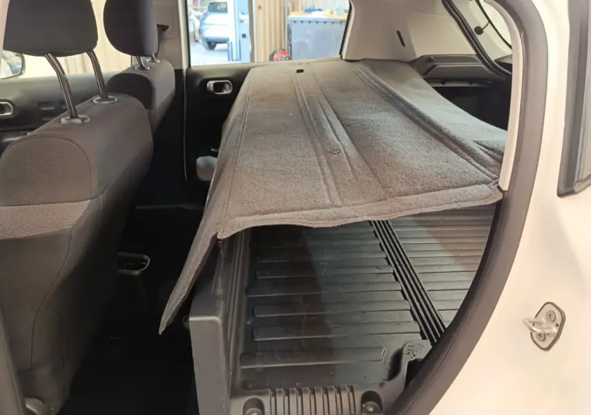 Vue intérieure côté droit du coffre ouvert d'une Citroën C3 blanche 2022 avec tapis de coffre relevé.