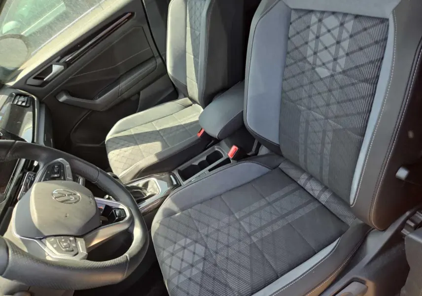Vue intérieure côté conducteur du Volkswagen T-Roc 2025 noir métal, sièges tissu gris à motifs et volant multifonction cuir.