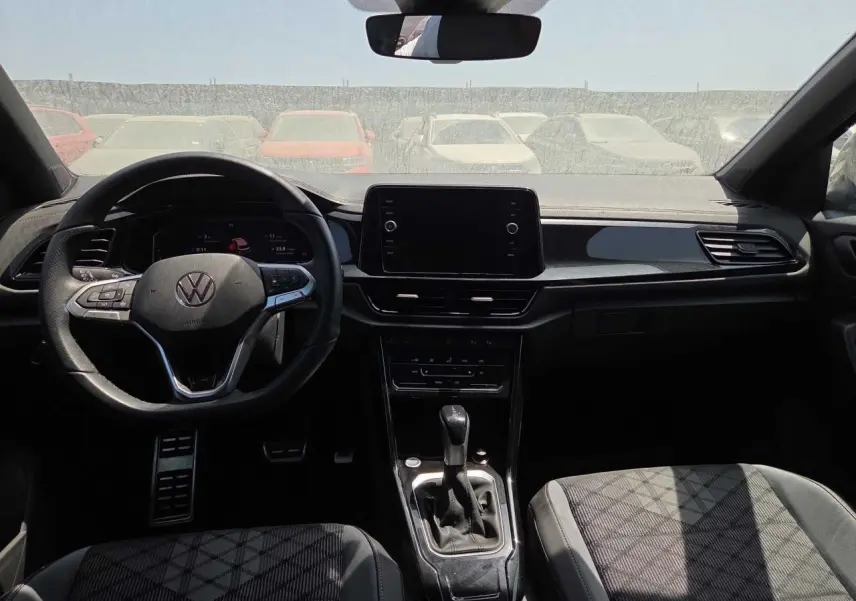 Vue intérieure avant du Volkswagen T-Roc noir métal 2025, avec volant multifonction et écran tactile central.