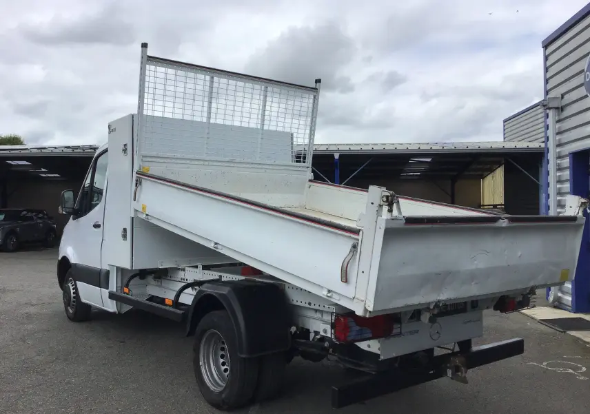 Mercedes Sprinter blanc 514 CDI en vue 3/4 arrière droit, avec benne basculante et coffre latéral visible.