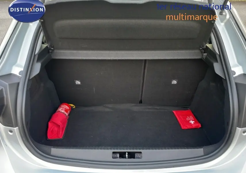 Coffre ouvert vu de l'arrière d'une Opel Corsa gris kristall metal, avec trousse de secours et extincteur rouge visibles.