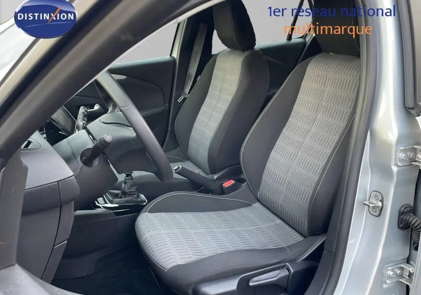 Vue intérieure côté conducteur de l’Opel Corsa gris kristall metal, montrant les sièges tissu gris et noir et la boîte manuelle.