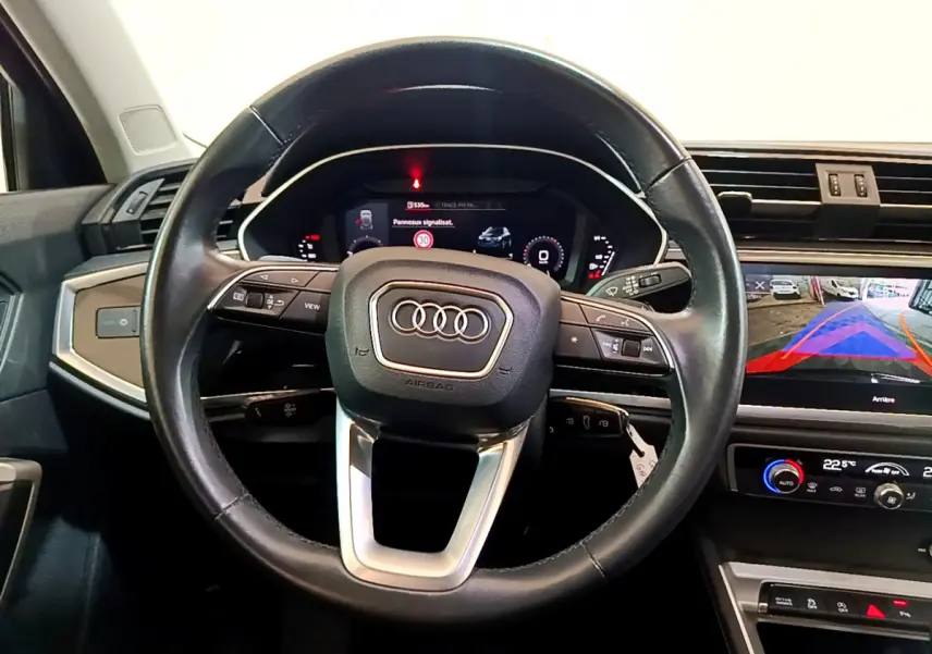 Vue intérieure centrée sur le volant cuir noir d’un Audi Q3 2021 avec tableau de bord numérique et écran tactile de recul.