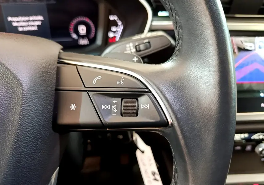 Gros plan sur les commandes gauche du volant cuir noir de l'Audi Q3 35 TDI 2021 avec affichage numérique en arrière-plan.
