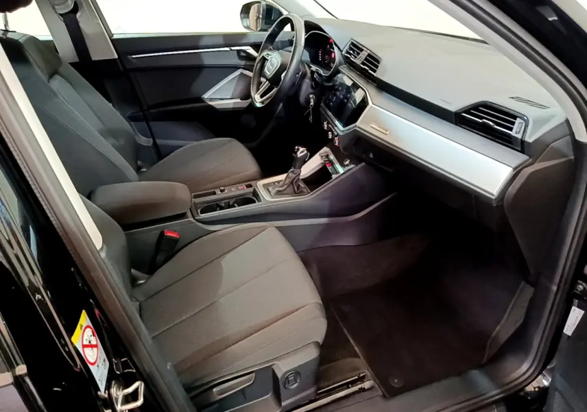 Intérieur côté conducteur d’un Audi Q3 noir 2021, montrant sièges tissu gris et tableau de bord moderne avec écran tactile.
