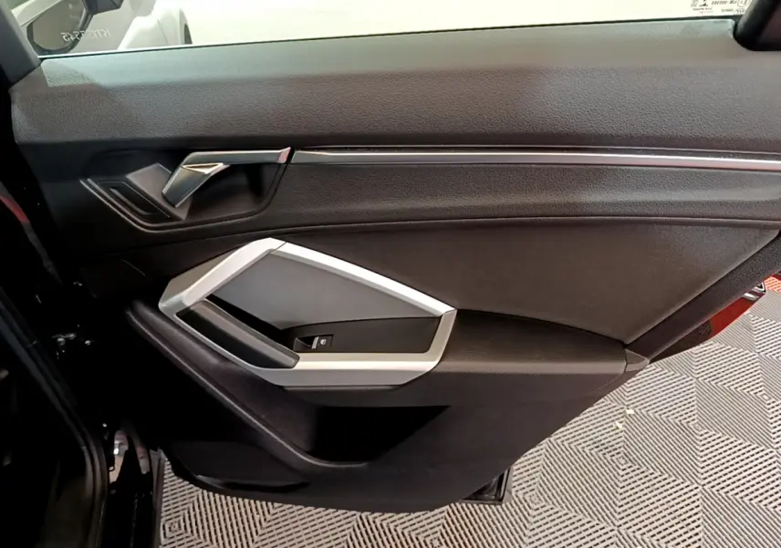 Vue rapprochée de la porte intérieure côté droit noire de l'Audi Q3 35 TDI 2021 avec poignée argentée.