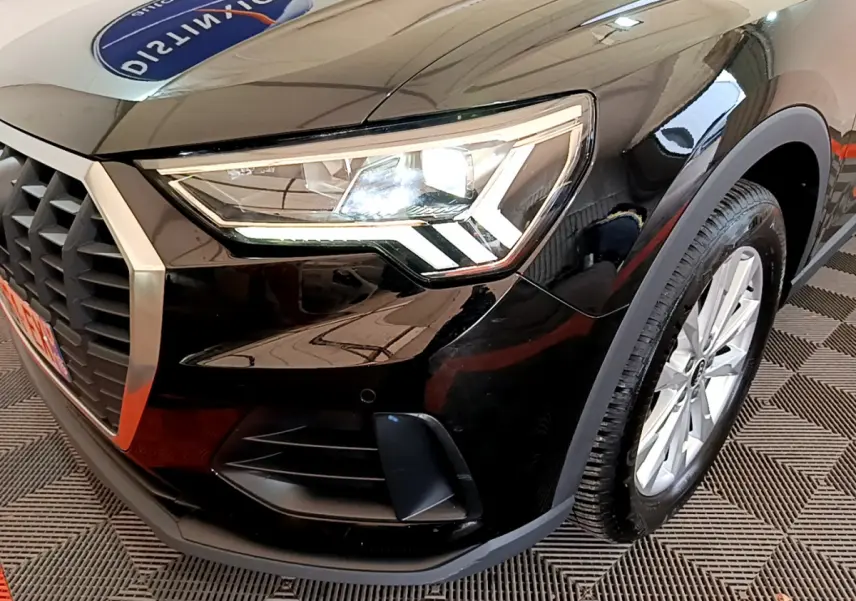 Gros plan sur l'avant droit noir de l'Audi Q3 35 TDI, mettant en valeur le phare LED et la calandre hexagonale.