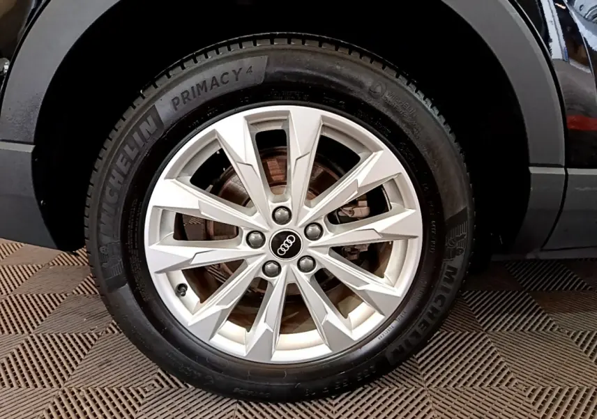 Gros plan sur la roue avant droite noire d'un Audi Q3 35 TDI 150 S tronic Business Line avec jante argentée à rayons fins.