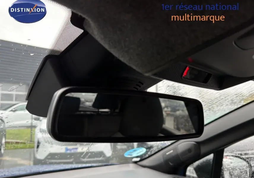 Vue intérieure centrée sur le rétroviseur intérieur d’un Renault Captur bleu Iron Metal avec toit noir sous la pluie.